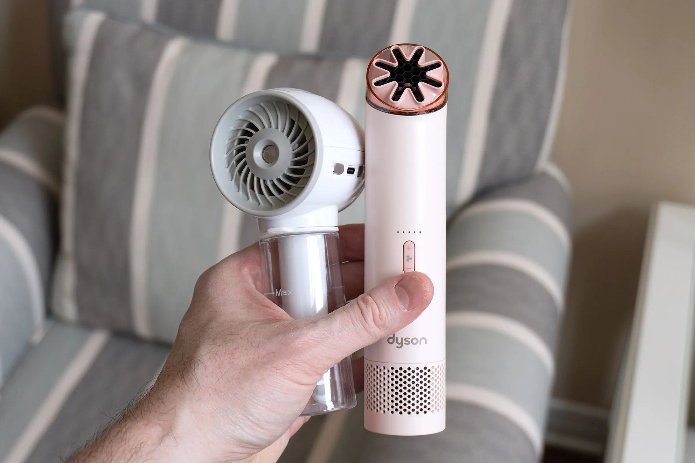 A hand holds up two handheld fans from Nitecore and Dyson.