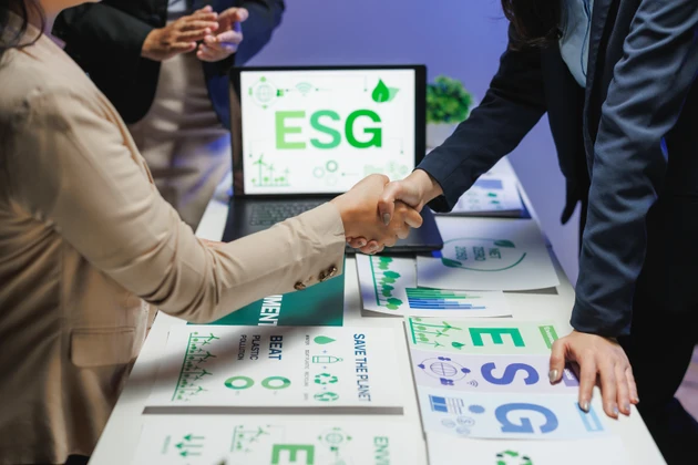 Businesswomen shaking hands on esg agreement with charts and laptop
