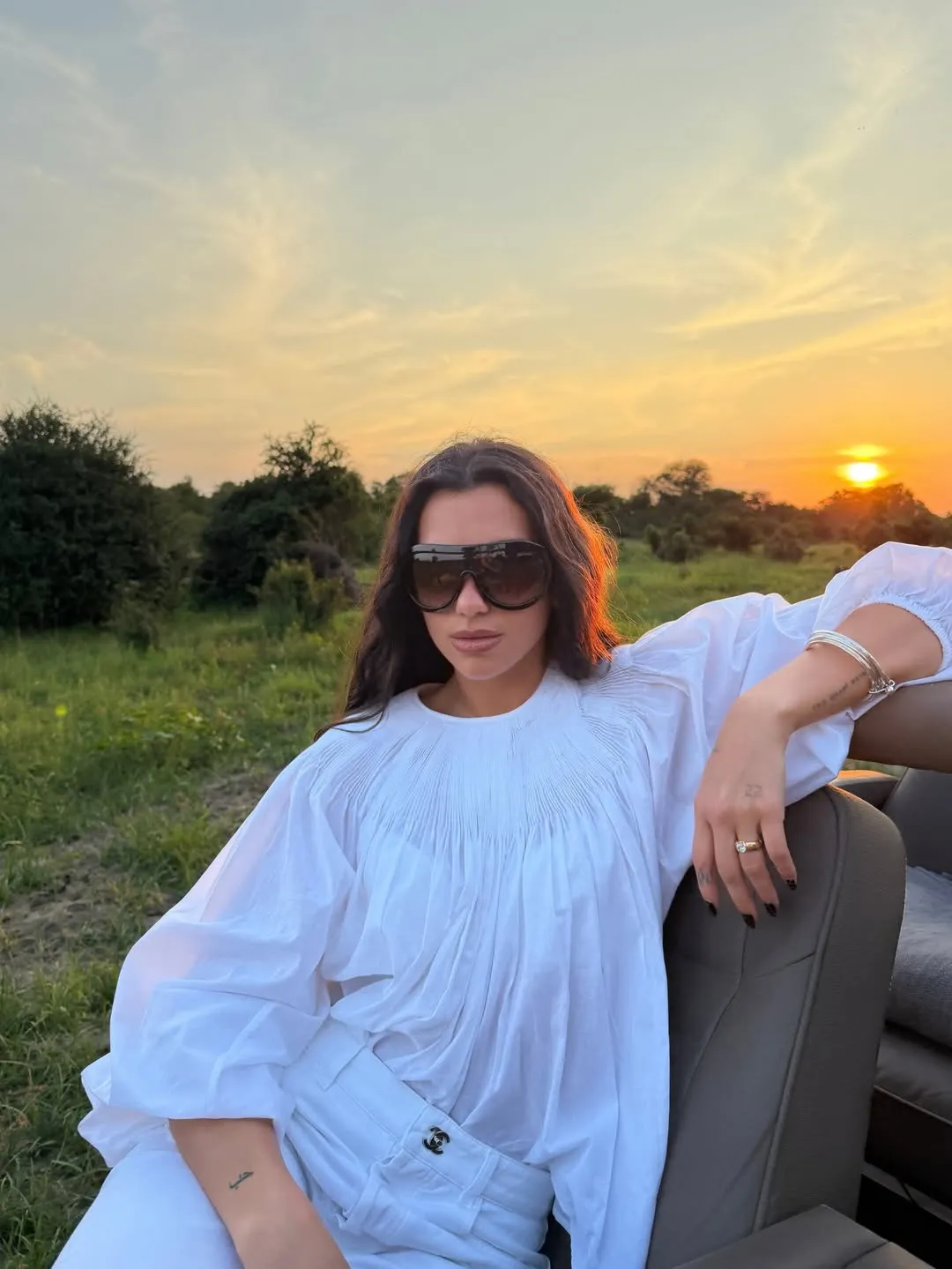 Image may contain Dua Lipa Clothing Sleeve Adult Person Sitting Brown Hair Hair Blouse Nature Outdoors and Sky