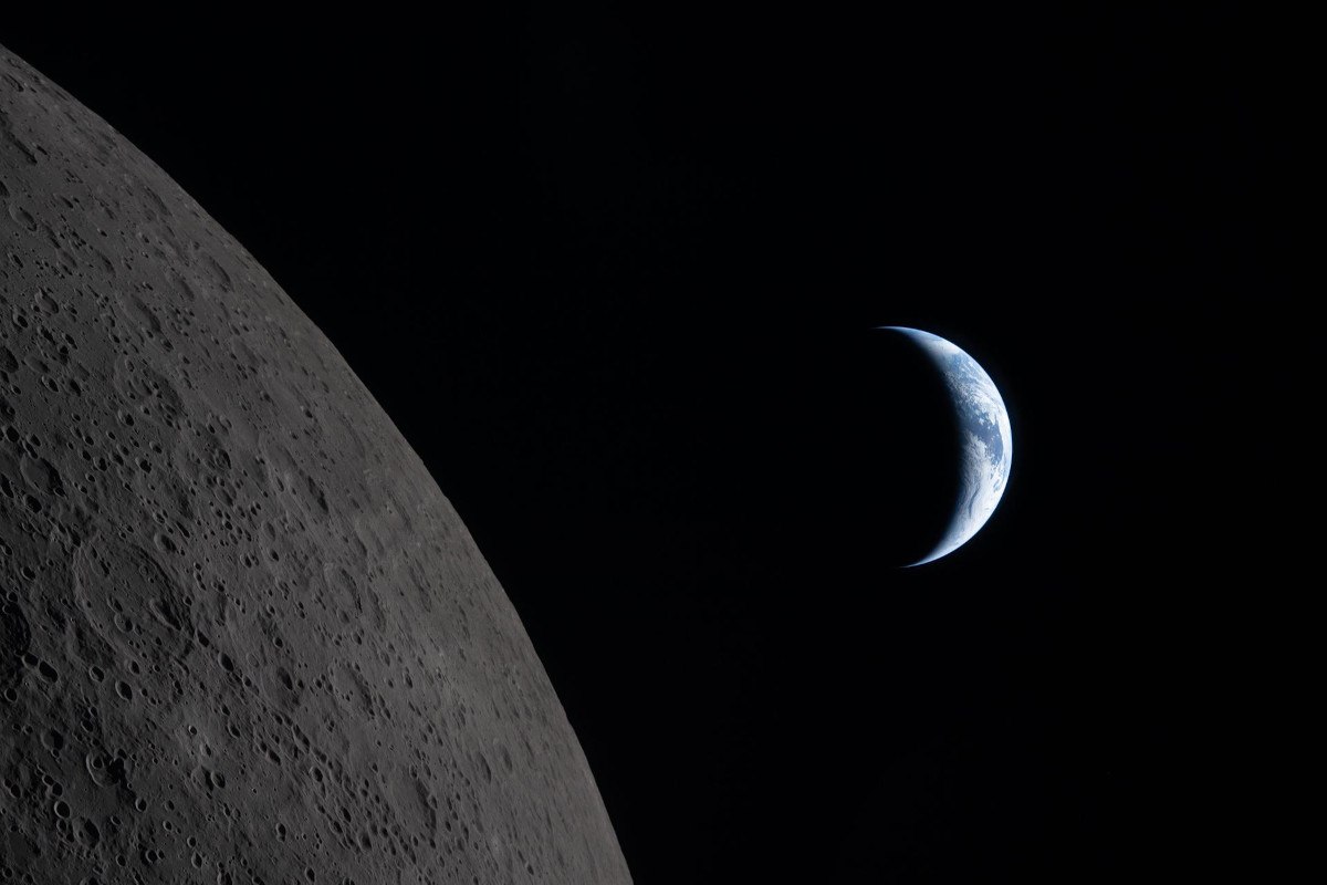 A picture taken of Earth in a crescent phase next to the grey darker side of the moon in space.
