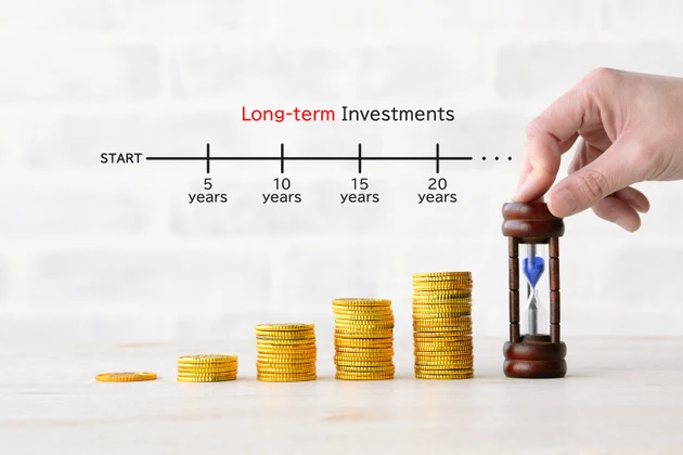 A person"s hand placing a pile of coins and an hourglass, image of long-term investment