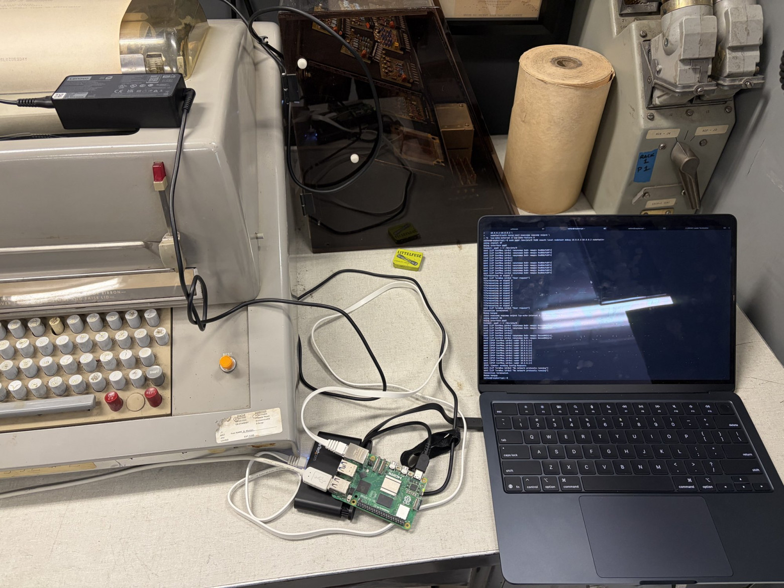 Сетевая конфигурация: Raspberry Pi с запущенным PPPD-мостом между Mac и последовательным портом UNIVAC. A workbench with the UNIVAC teletype on the left, a Raspberry Pi in the middle, and a Mac laptop on the right.