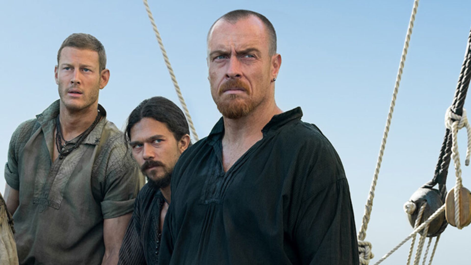 Three pirates stand on a boat looking out to sea