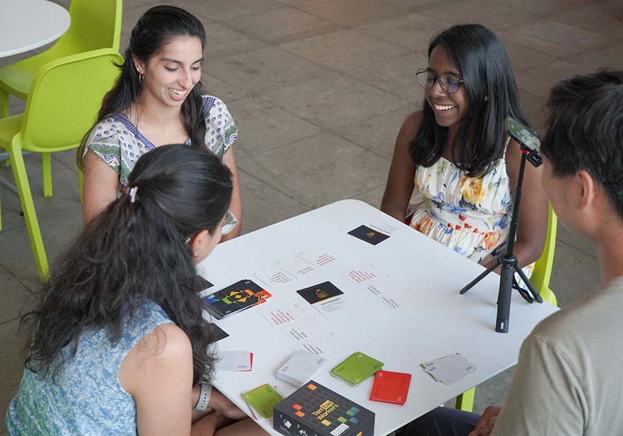 Four people sit around a table, playing a card game.