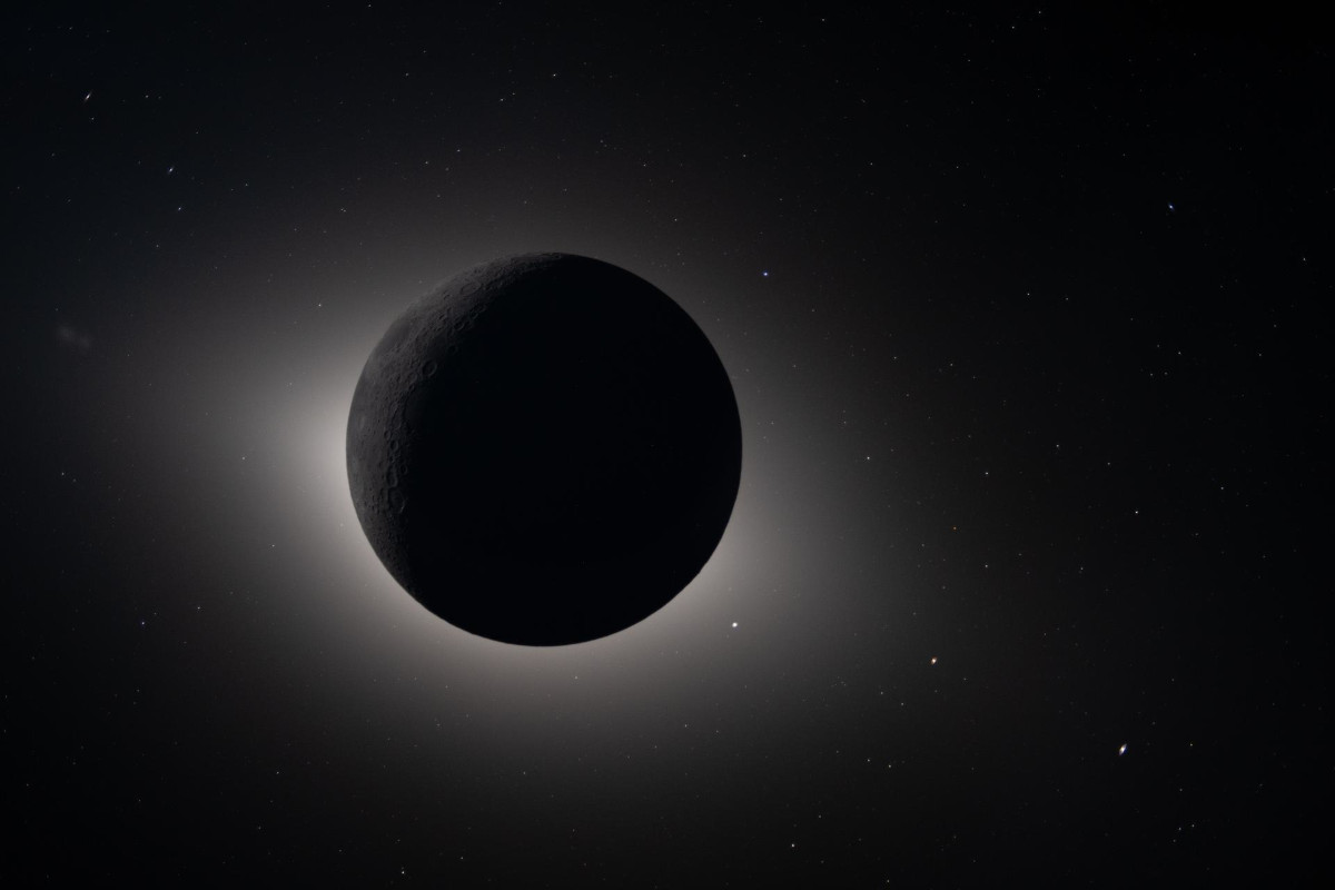 An image of the moon covering the face of the sun in space. A faint bright halo can be seen around a dark moon.