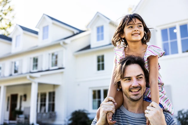 Young girl riding on her fathers shoulders in front of suburban home