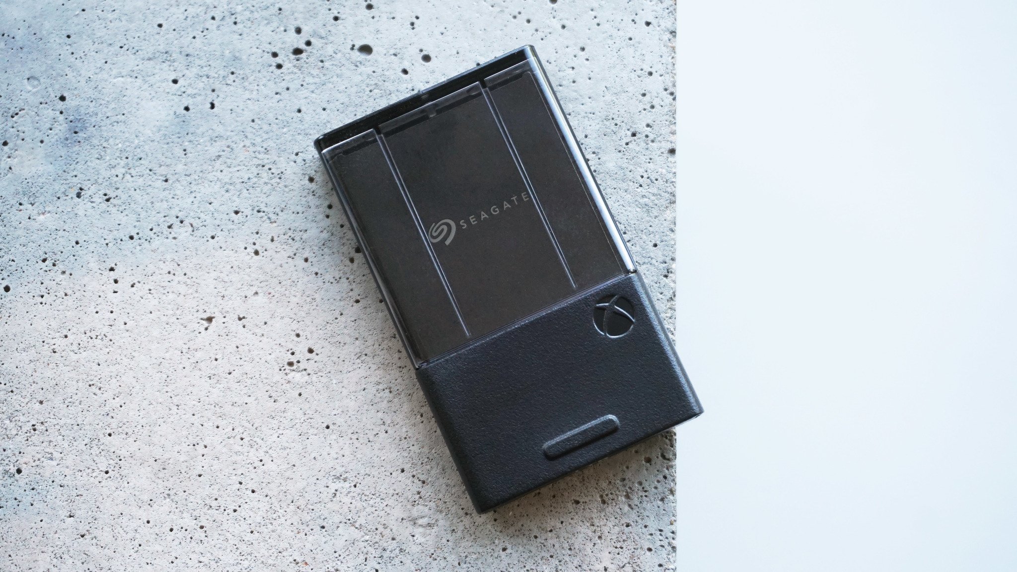 A Seagate Xbox storage expansion card rests on a speckled gray concrete surface. The card has a sleek black exterior and minimalist design.