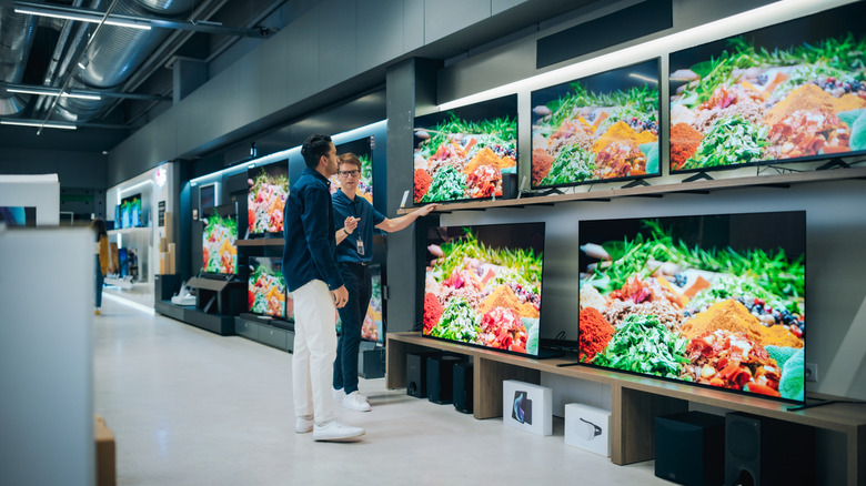 A man speaking with sales associate at a TV display in an electronics store