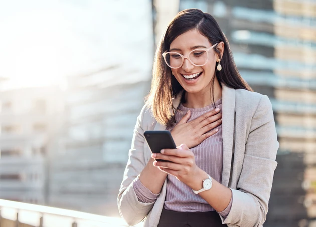 Shot of an attractive young businesswoman standing alone outside and looking surprised while using her cellphone