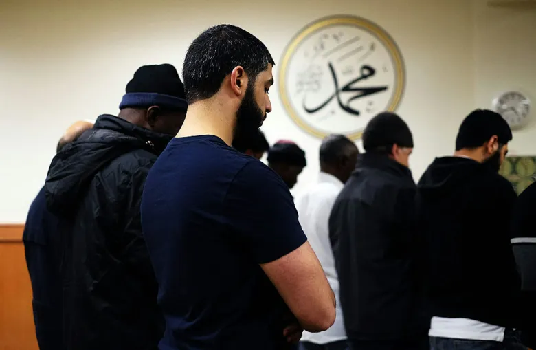 Many men stand in rows, praying with their heads bowed.